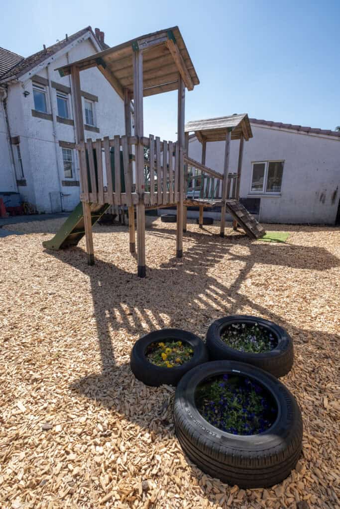 Bright outdoor play area at Thrive Childcare with wooden play structures, rubber tires for planting flowers, and a safe, engaging environment for young children to explore and grow.