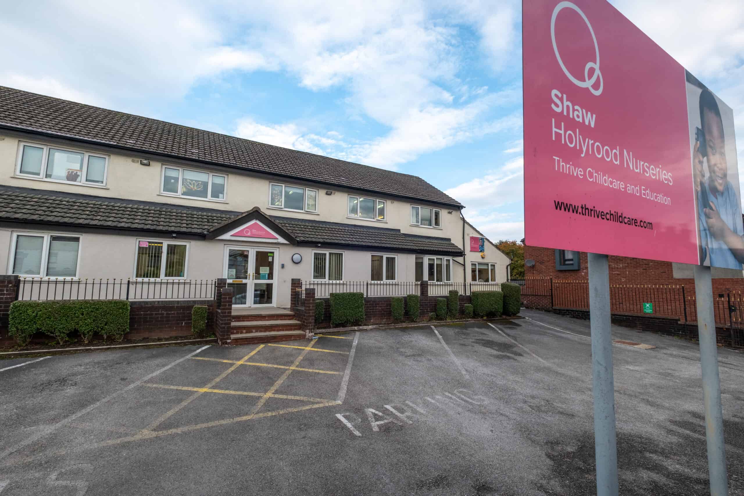Bright exterior of Thrive Childcare centre at Shaw Holyrood Nurseries with parking area and prominent pink signage showcasing childcare and early education services.