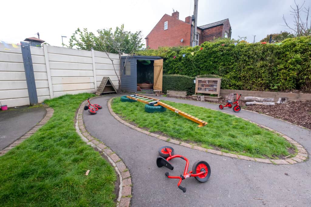 Bright outdoor play area with children's tricycles, climbing toys, and garden shed at Thrive Childcare, perfect for early childhood outdoor activities and developing motor skills in a safe environment.