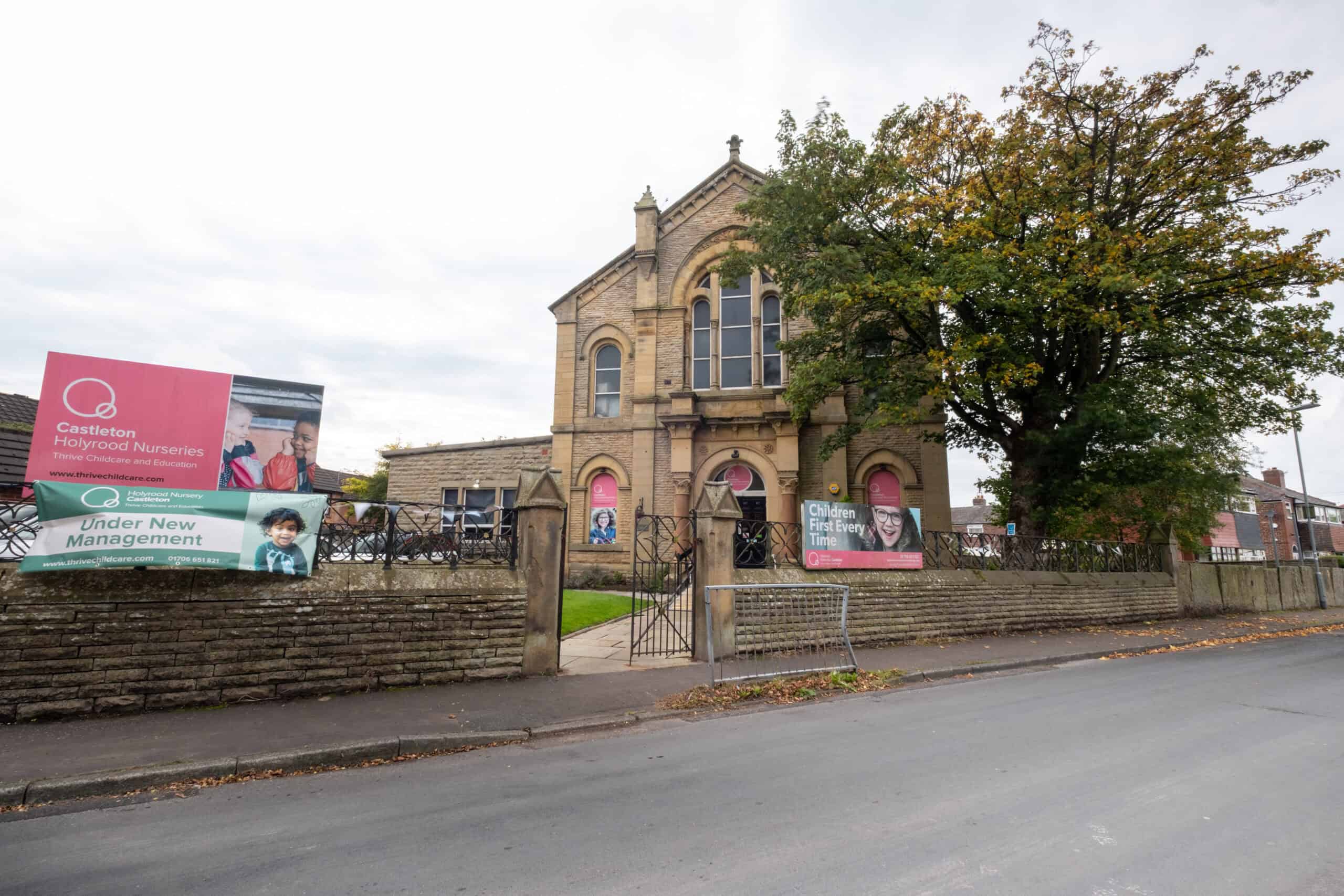 Bright, historic church building serving as Thrive Childcare facility with signage highlighting nursery and education services in Castleton, under new management, colourful exterior, and surrounding trees.