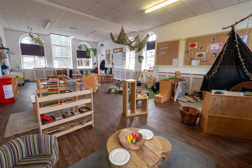 Bright and spacious indoor childcare playroom with natural light, wooden toys, cosy tent, and educational displays, designed for early childhood development and safe play at Thrive Childcare.