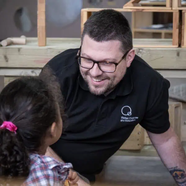 A caring childcare professional engaging with a young girl in a colourful classroom setting at Thrive Childcare, promoting early childhood education and development.