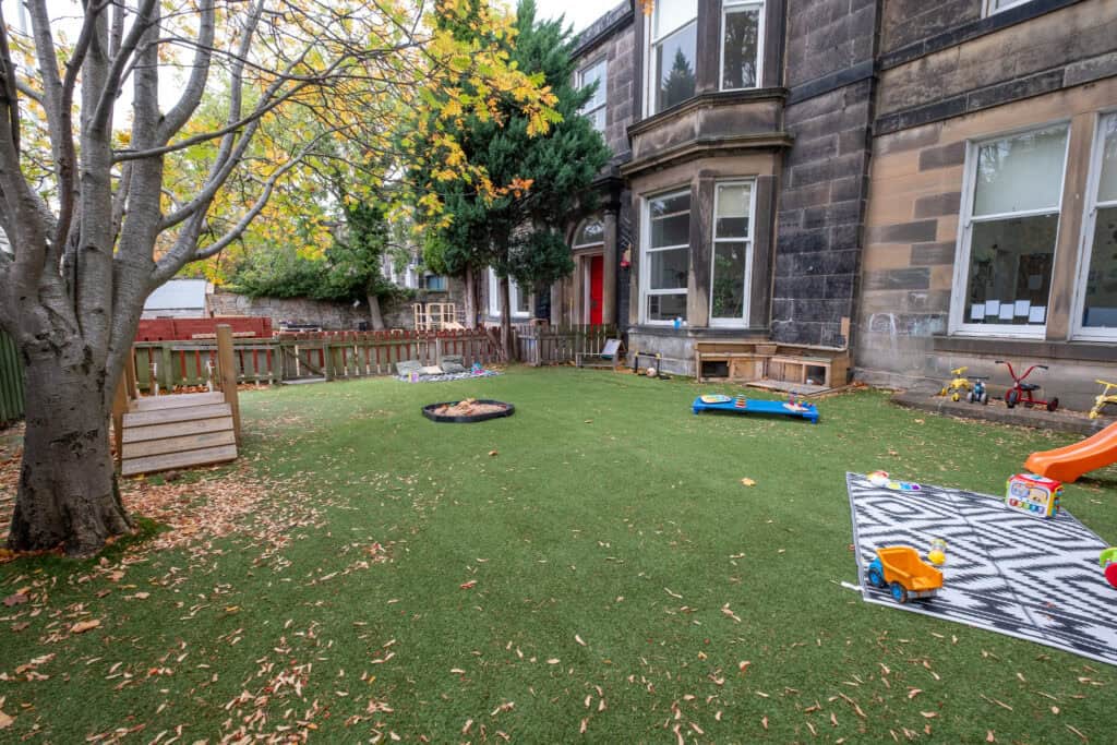 Bright outdoor childcare play area with soft grass, toys, and autumn leaves, perfect for learning and fun at Thrive Childcare. Safe, nurturing environment for young children’s outdoor activities.