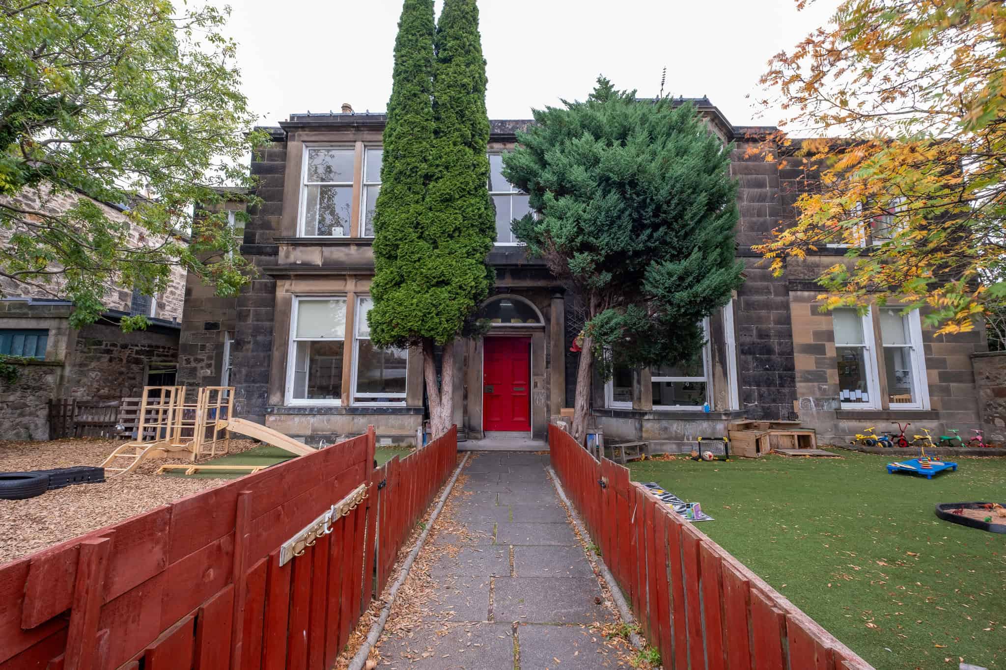 Bright, welcoming childcare centre entrance with colourful outdoor play area and lush trees, promoting a safe and engaging environment for children's growth and development at Thrive Childcare.