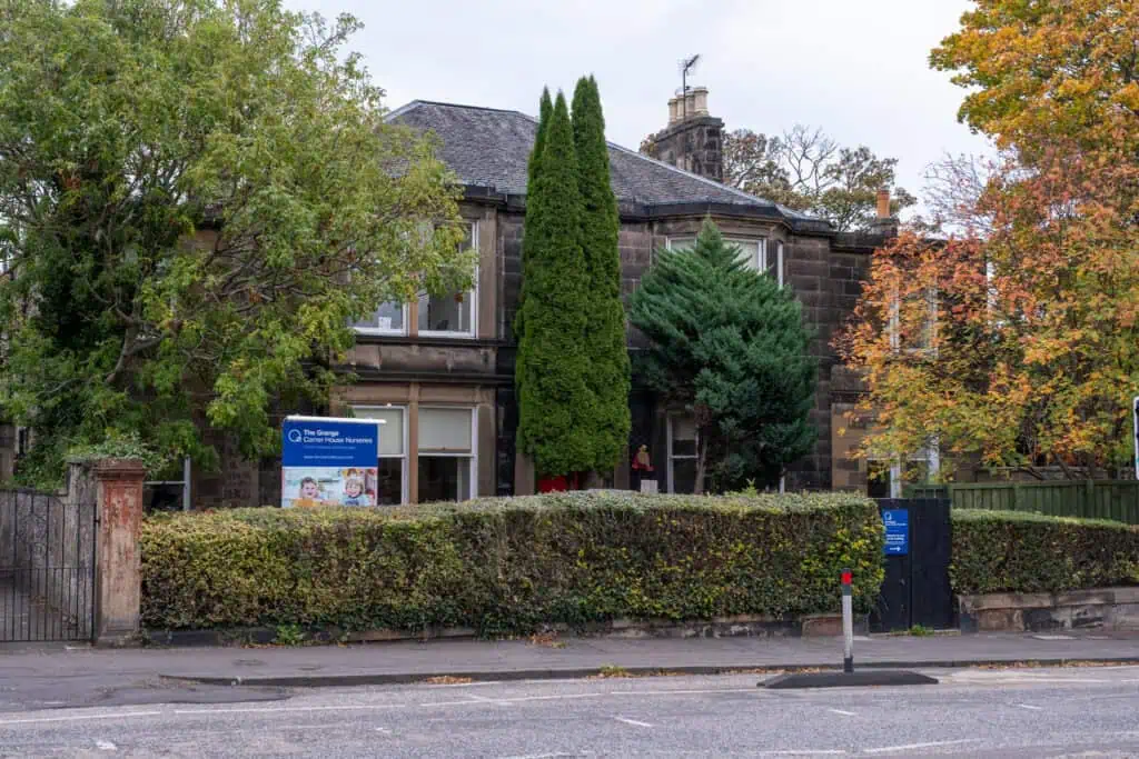 Bright, welcoming nursery building surrounded by lush trees and greenery, featuring a colourful sign for Thrive Childcare, providing high-quality early childhood education and nursery care in a friendly environment.
