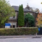 Bright, welcoming nursery building surrounded by lush trees and greenery, featuring a colourful sign for Thrive Childcare, providing high-quality early childhood education and nursery care in a friendly environment.