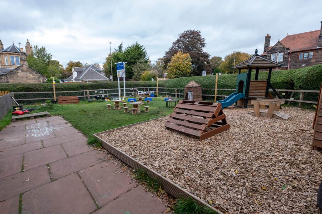 A colourful outdoor childcare playground at Thrive Childcare, featuring wooden play equipment, slides, seating, and a safe outdoor area for young children to learn and play.
