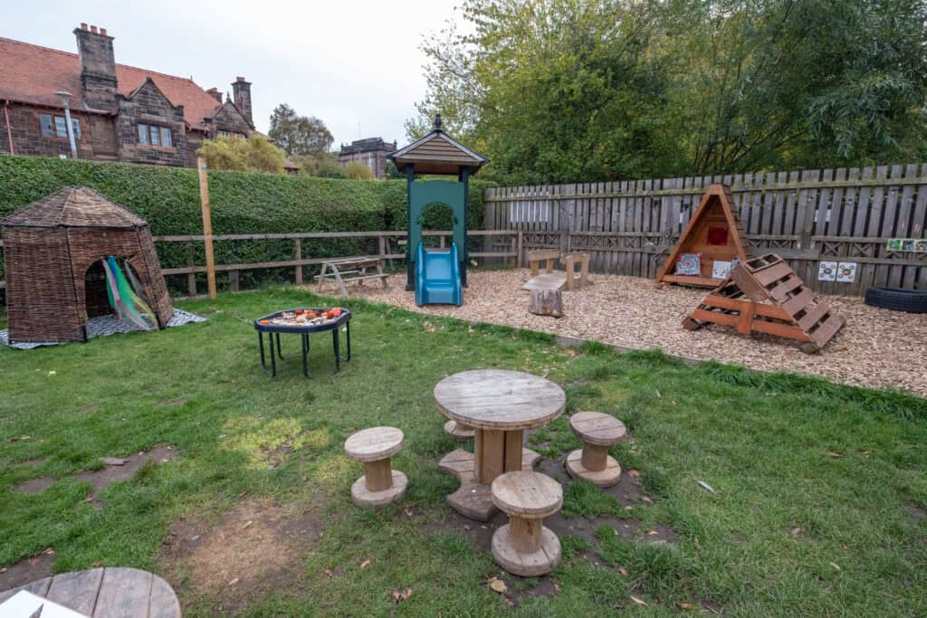 Bright outdoor children's playground at Thrive Childcare, featuring a slide, playhouse, sandpit, and woodland area for active kids' fun and learning.