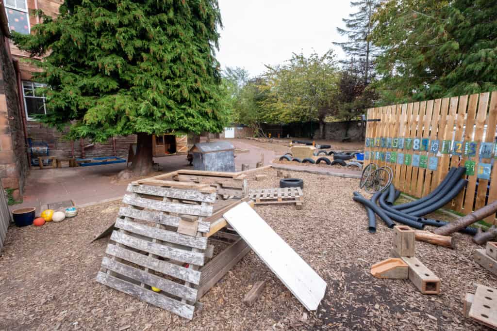 A colourful outdoor play area at Thrive Childcare with natural wooden structures, trees, and sensory toys for children’s outdoor learning and development.