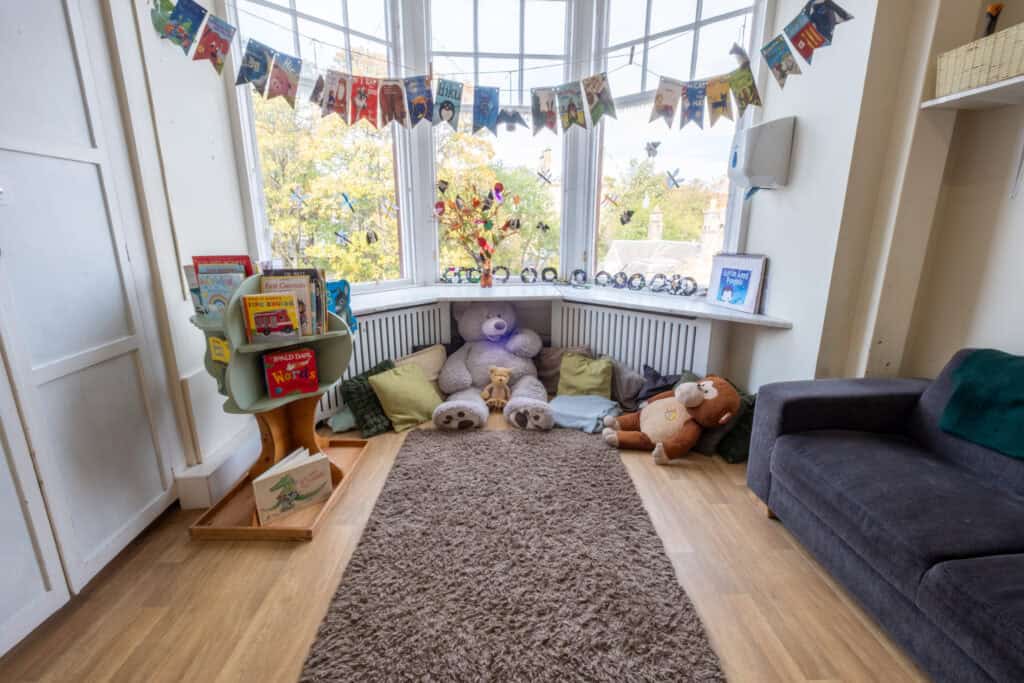 Bright indoor play area at Thrive Childcare with plush toys, cushions, children's books, colourful decorations, and large windows letting in natural light for a welcoming early childhood education environment.