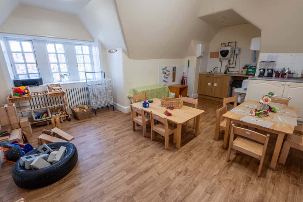 Bright inclusive childcare playroom with wooden tables, toys, and learning materials, ideal for young children. Spacious, well-lit, safe environment designed for early childhood development and educational activities.