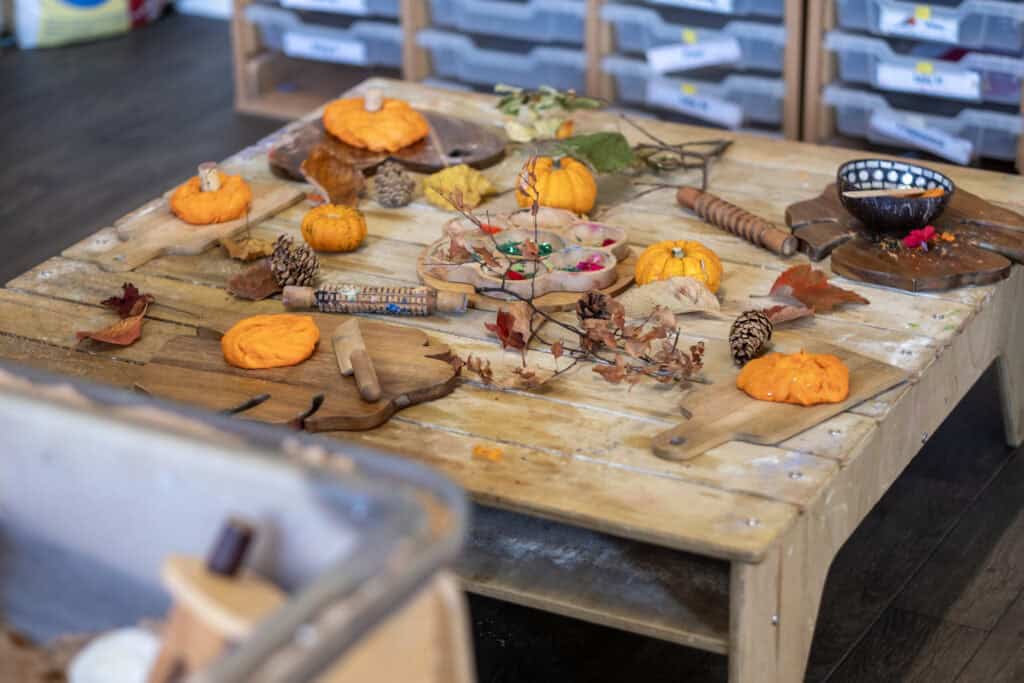 1. Children’s autumn-themed craft table with pumpkins, leaves, pinecones, and decorative paint, perfect for preschool arts and crafts activities.