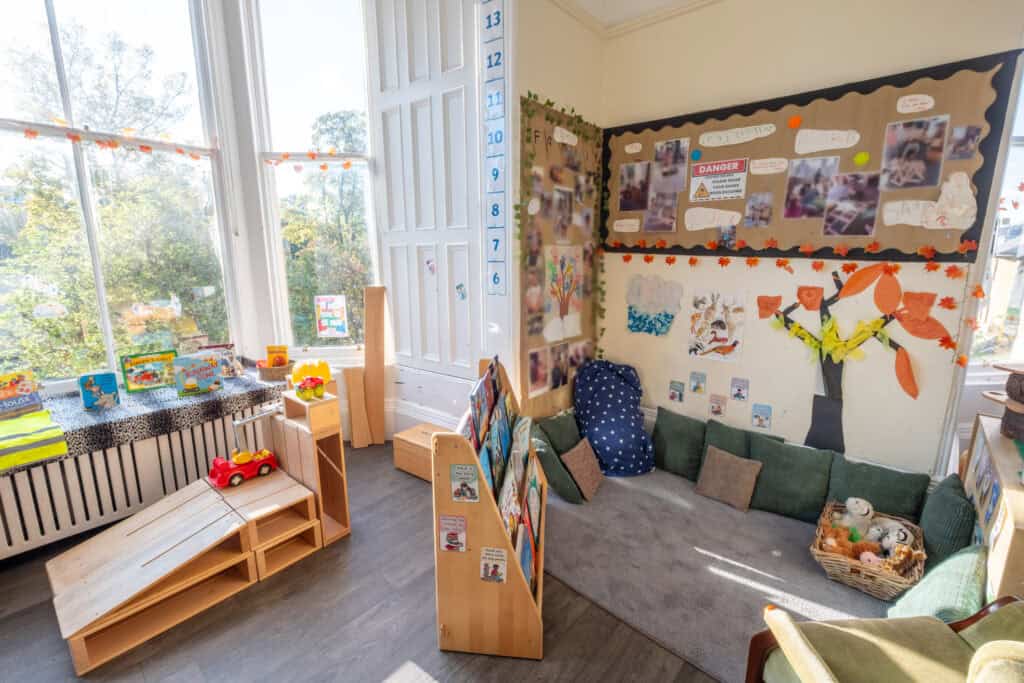 Bright childcare playroom with books, toys, and educational displays at Thrive Childcare, featuring a cosy reading corner and large windows for natural light, fostering learning and early childhood development.