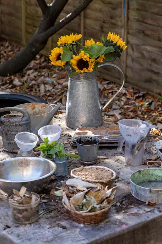 Bright sunflower bouquet in a rustic metal jug on an outdoor garden table with gardening tools and soil, highlighting outdoor activities at Thrive Childcare.