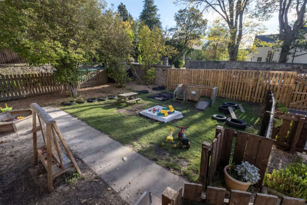 Bright outdoor play area at Thrive Childcare with toys, sandpit, slides, and garden fencing, perfect for children to explore and enjoy outdoor activities in a safe environment.