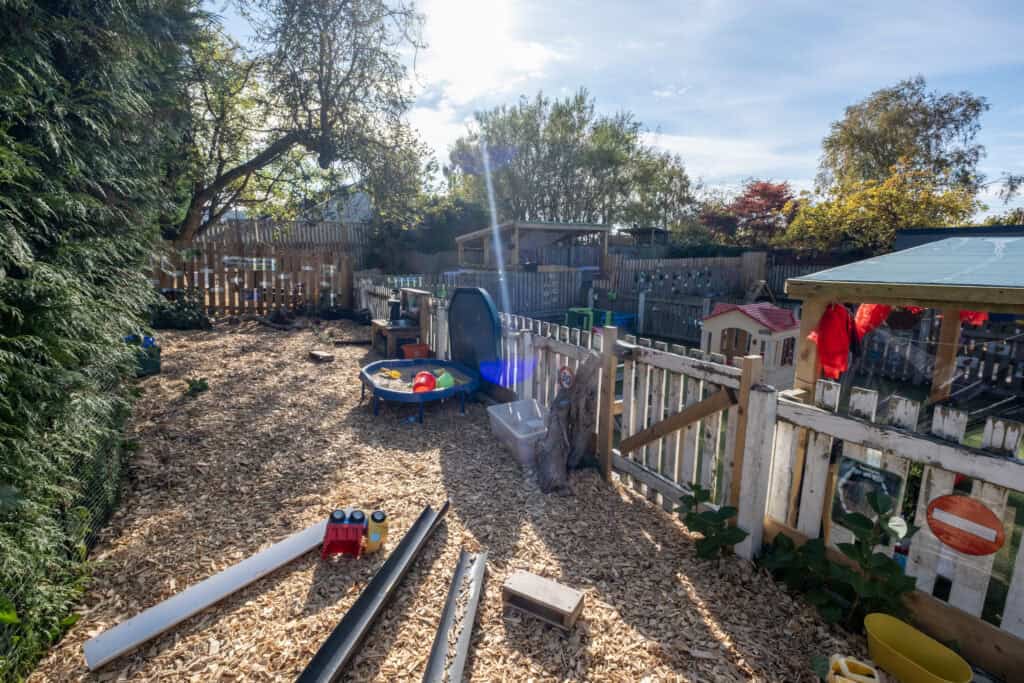 Bright outdoor early childhood play area at Thrive Childcare, featuring wooden fences, sensory toys, and natural elements for children’s outdoor learning and development.