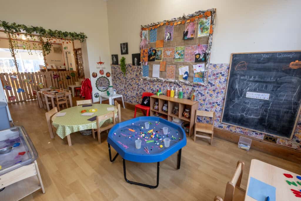 Bright and welcoming childcare classroom with arts and crafts area, sensory tables, and colourful decorations, designed for early childhood development and learning at Thrive Childcare.
