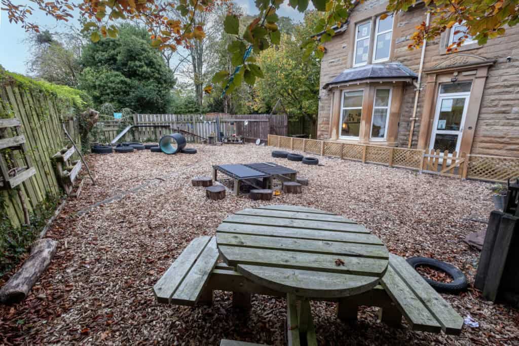 Soft fall playground area at Thrive Childcare with wooden outdoor furniture, tires, and play equipment, designed for children’s outdoor activities and safe play in a natural environment.