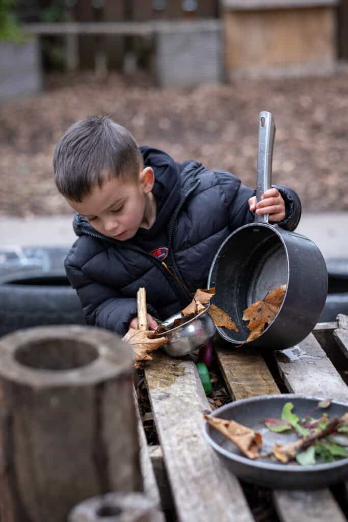 A young child playing outdoors in a childcare setting, exploring with leaves and outdoor toys, enhancing learning and development at Thrive Childcare.