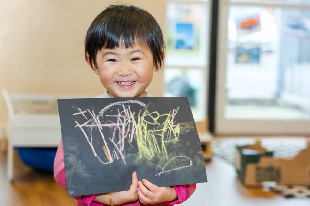 Happy smiling child holding colourful chalk drawing at Thrive Childcare, fostering early childhood development, creativity, and learning in a nurturing environment, ideal for parents seeking quality childcare services in en_GB.