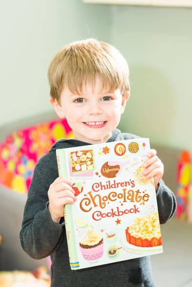 A happy young boy holding a children's chocolate cookbook at Thrive Childcare, promoting fun learning activities for kids.