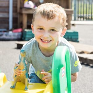 Bright happy young boy playing outside at Thrive Childcare with toy dinosaur, showcasing friendly childcare environment and outdoor activities for early childhood development.