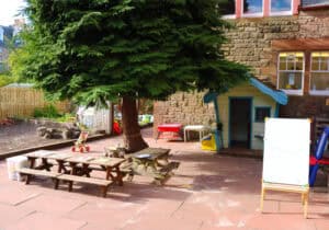 Bright outdoor play area at Thrive Childcare with picnic tables, a small treehouse, and colorful toys, providing a safe and engaging environment for children’s outdoor activities and learning.