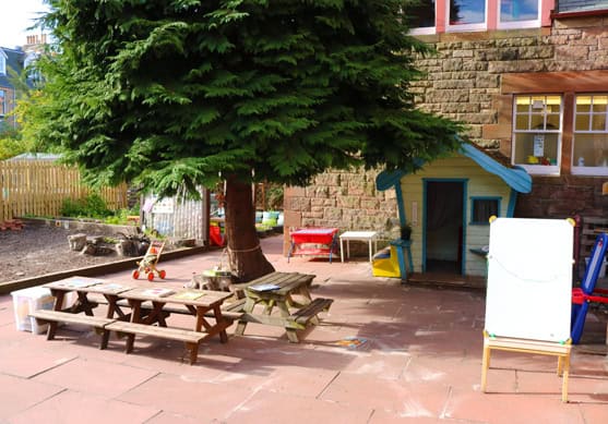 Bright outdoor play area at Thrive Childcare with picnic tables, a small treehouse, and colorful toys, providing a safe and engaging environment for children’s outdoor activities and learning.