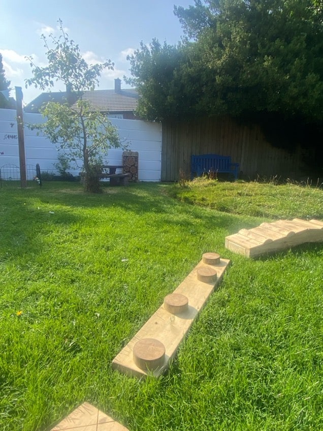Outdoor play area with wooden climbing logs and lush green grass at Holyrood Nursery Swinton.