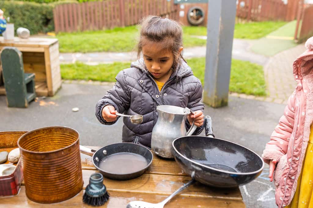 1. Young girl playing outdoors with kitchen toys at Thrive Childcare, engaging in imaginative role-play, promoting early childhood development and social skills.