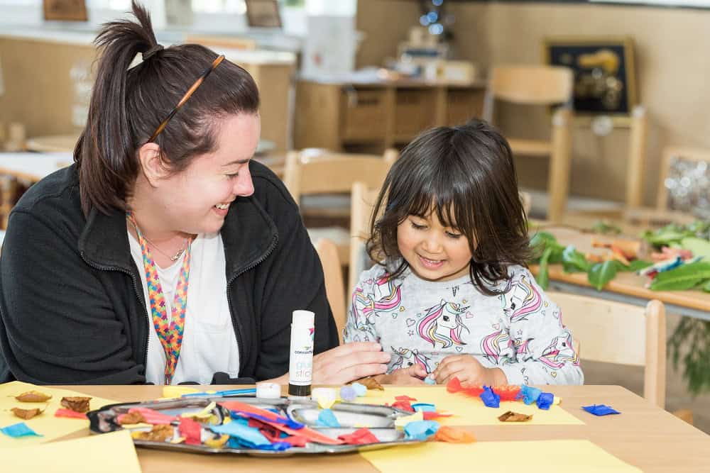 Happy childcare teacher and young girl engaging in arts and crafts activity at Thrive Childcare, promoting early childhood development, creativity, and a nurturing learning environment.