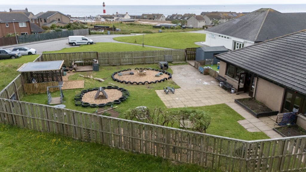 Bright outdoor play area at Thrive Childcare with sandpits, tire obstacle courses, and climbing structures in a secure, fenced yard near the coast, offering a safe, engaging environment for children's outdoor activities.