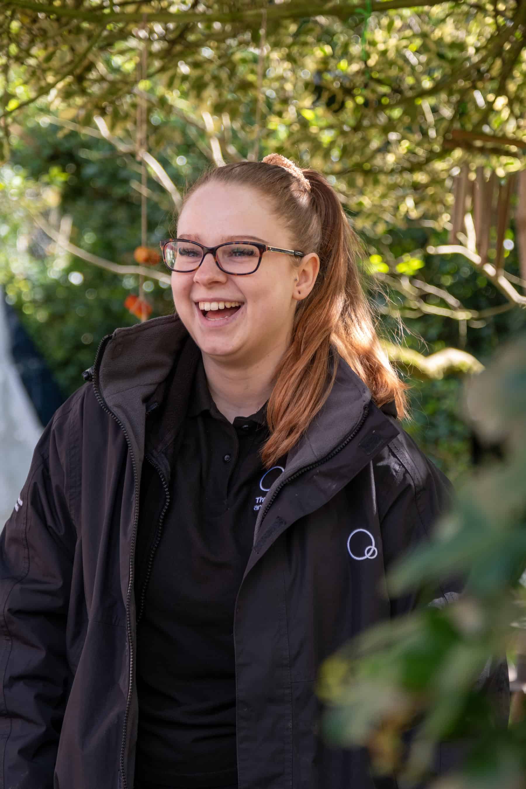 A smiling caregiver at Thrive Childcare engaging with children outdoors in a lush garden setting.