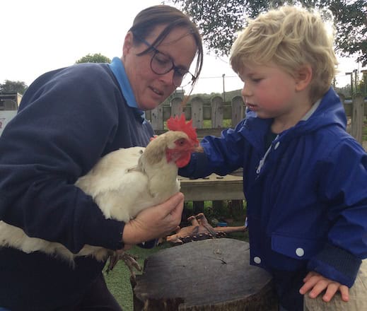 Friendly female caregiver interacting with a young boy and a chicken at Thrive Childcare, promoting outdoor learning and animal interaction for early childhood development.
