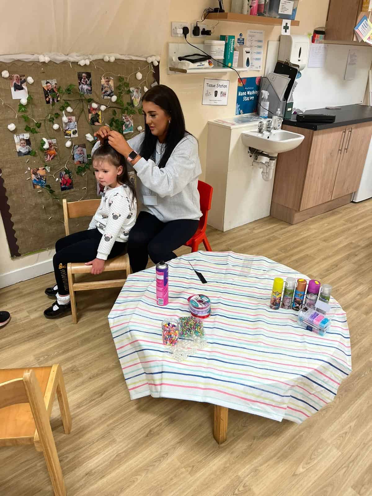 Bright indoor scene of a childcare centre with a caregiver styling a young child's hair, educational and nurturing environment, Thrive Childcare, early childhood education, caring childcare service.