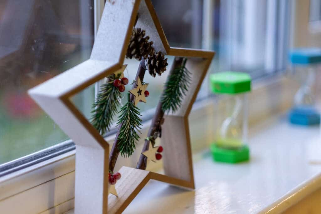 A festive star-shaped decoration with pine branches and holiday ornaments on a windowsill.