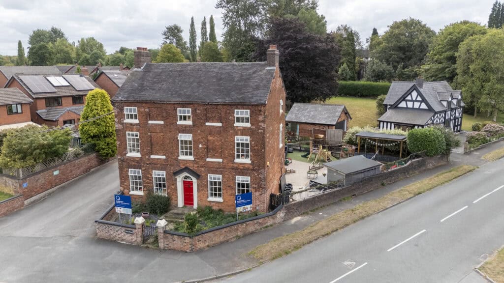 Bright red door of Thrive Childcare, located in a charming brick building on a quiet residential street, with outdoor play areas and surrounding lush greenery, offering quality childcare services.