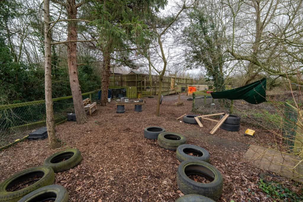 Outdoor play area with tires, wooden structures, and natural surroundings at Thrive Grosvenor House childcare centre.
