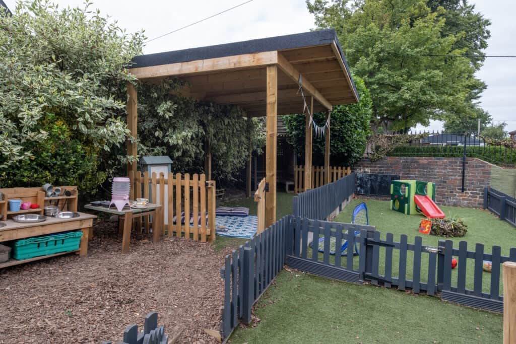 Colourful outdoor play area at Thrive Childcare, featuring a sandbox, slide, and garden lawn with safety fencing, ideal for early childhood development and outdoor activities in a safe environment.
