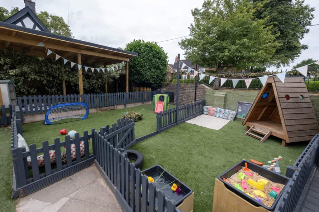 Bright outdoor children’s play area at Thrive Childcare with a sandbox, slide, sports toys, and wooden playhouse, designed for safe, fun-filled early childhood development and learning activities.