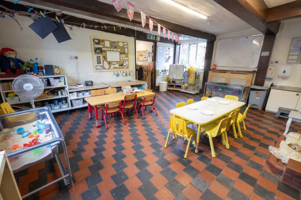 Playroom of a childcare centre with colourful tables and chairs, learning resources, toys, and a whiteboard, offering a safe and engaging environment for early childhood development and educational activities.