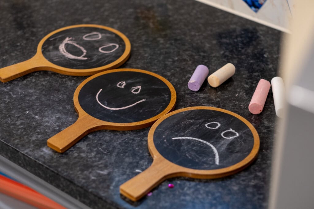 Bright smiley face and sad face chalkboard signs for childcare emotional learning, smiley faces for children's social-emotional development, colourful chalks for kids' educational activities.
