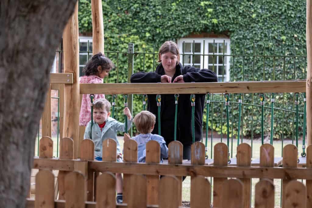 A group of young children and a caregiver enjoy outdoor playtime on a wooden balance platform at Thrive Childcare, promoting active learning and child development in a safe outdoor environment.