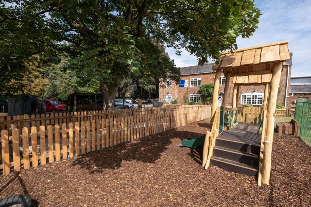 Bright outdoor play area at Thrive Childcare with a wooden slide, lush trees, and secure fencing, providing a safe, engaging environment for young children to explore and enjoy nature.