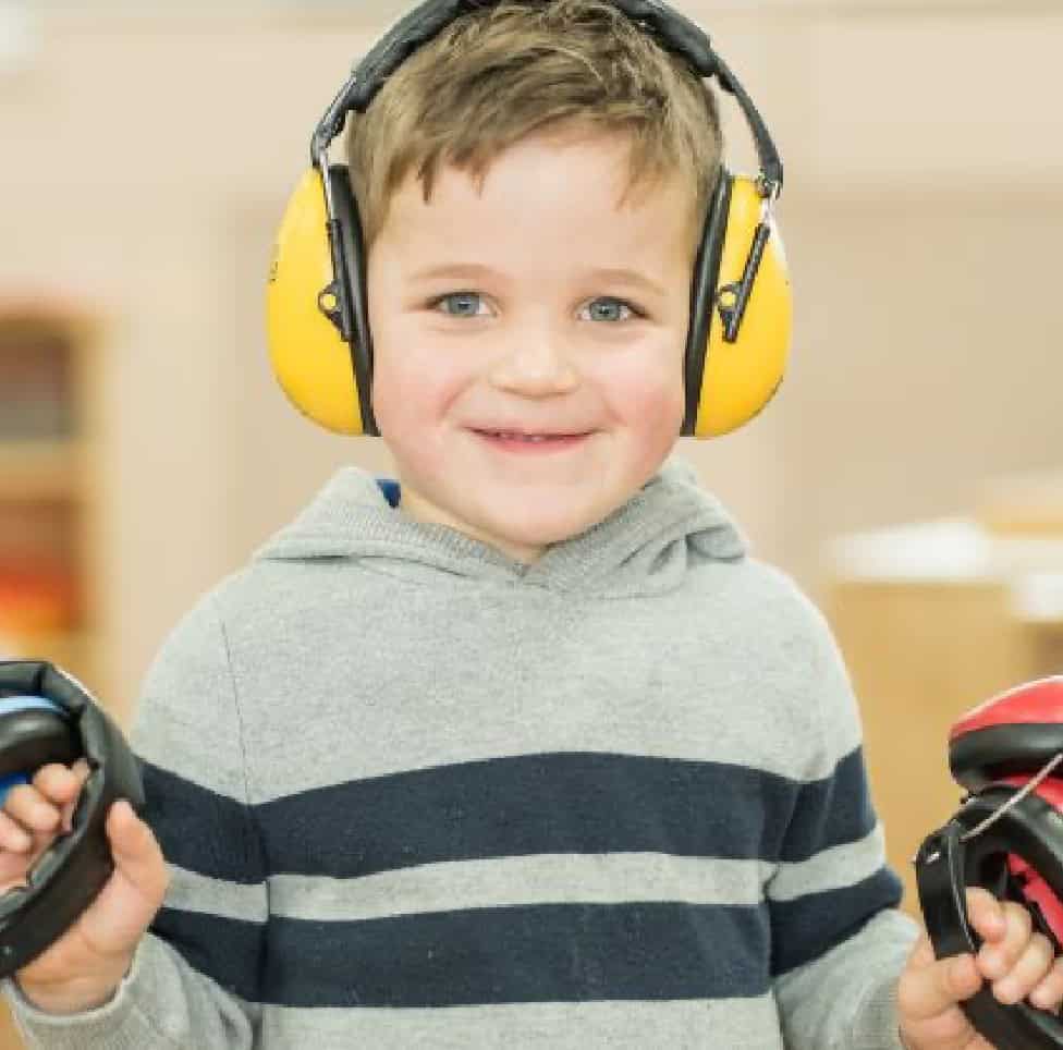 1. Child at Thrive Childcare wearing headphones, engaging in early childhood education, smiling and enjoying a creative activity.