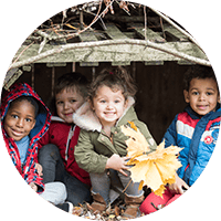 Brightly dressed children playing outdoors under a wooden shelter, enjoying autumn leaves and outdoor activities at Thrive Childcare.