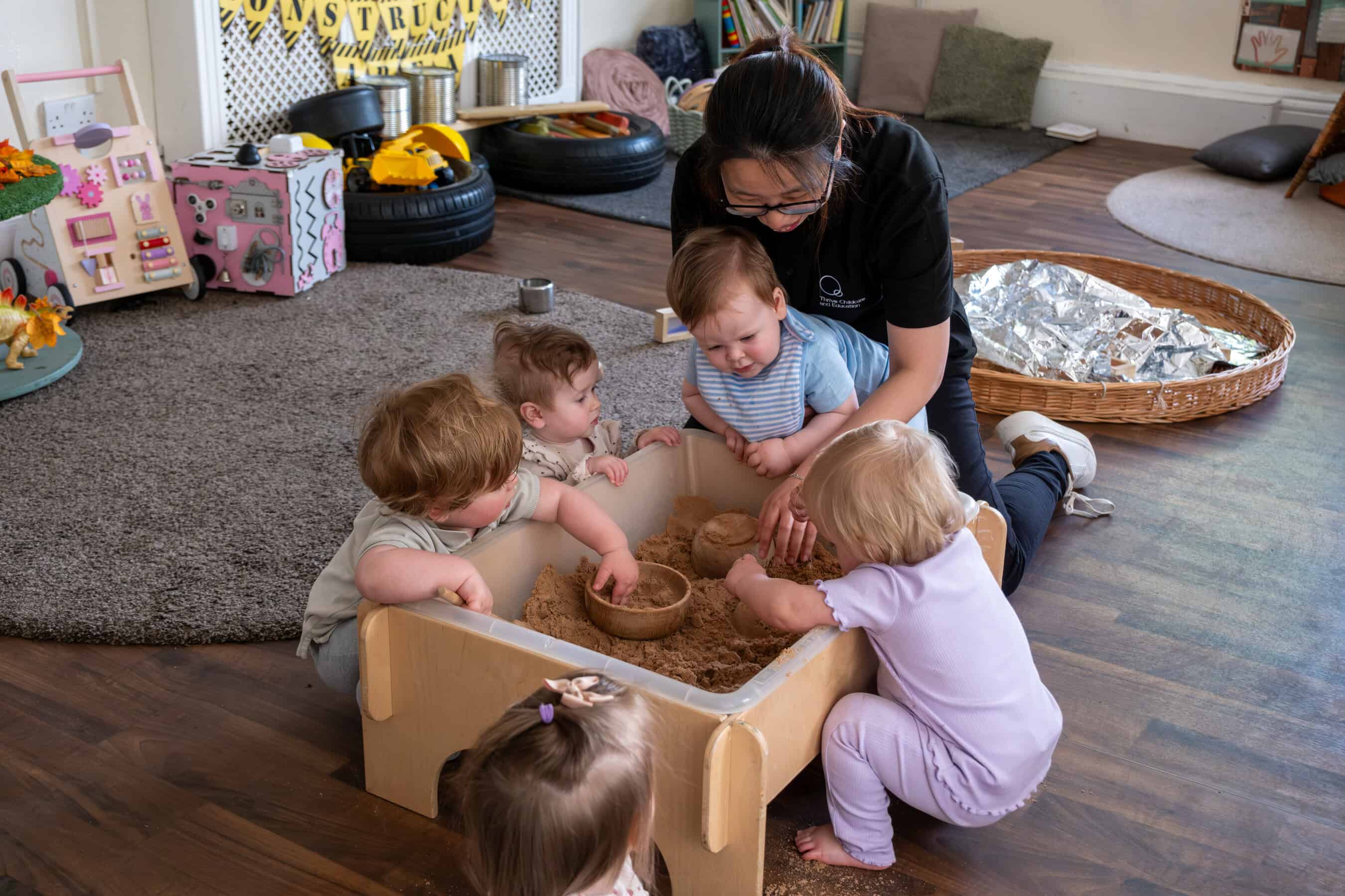 Children's indoor play area at Thrive Childcare with a teacher engaging kids in sensory sand activity, promoting early childhood development and learning through creative play.