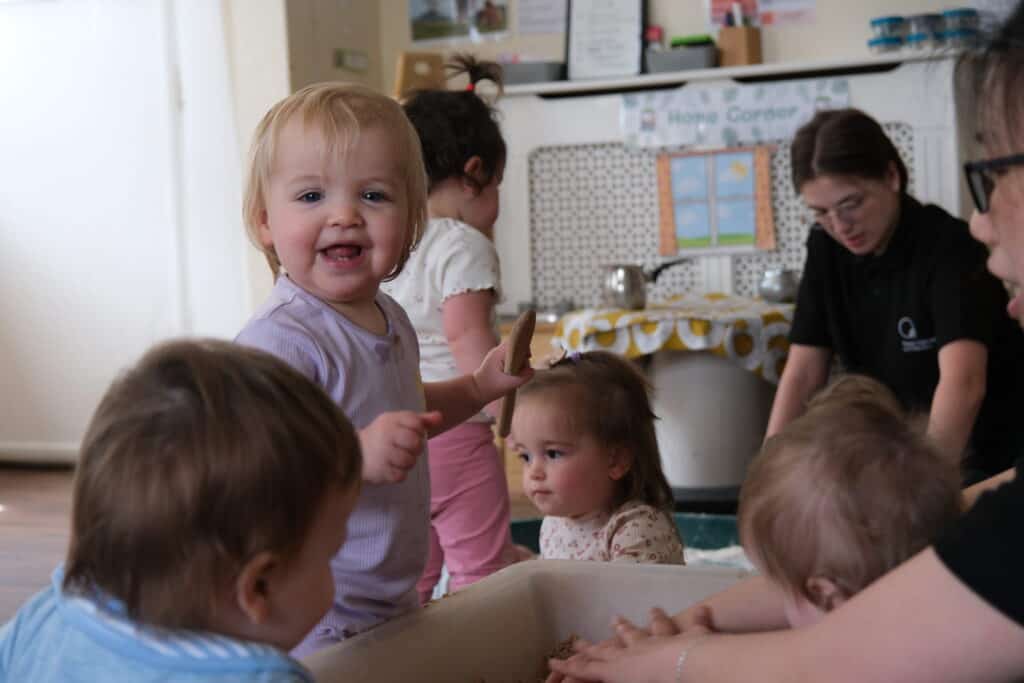 A happy toddler girl with blonde hair smiling and playing with a cookie in a childcare setting at Thrive Childcare.