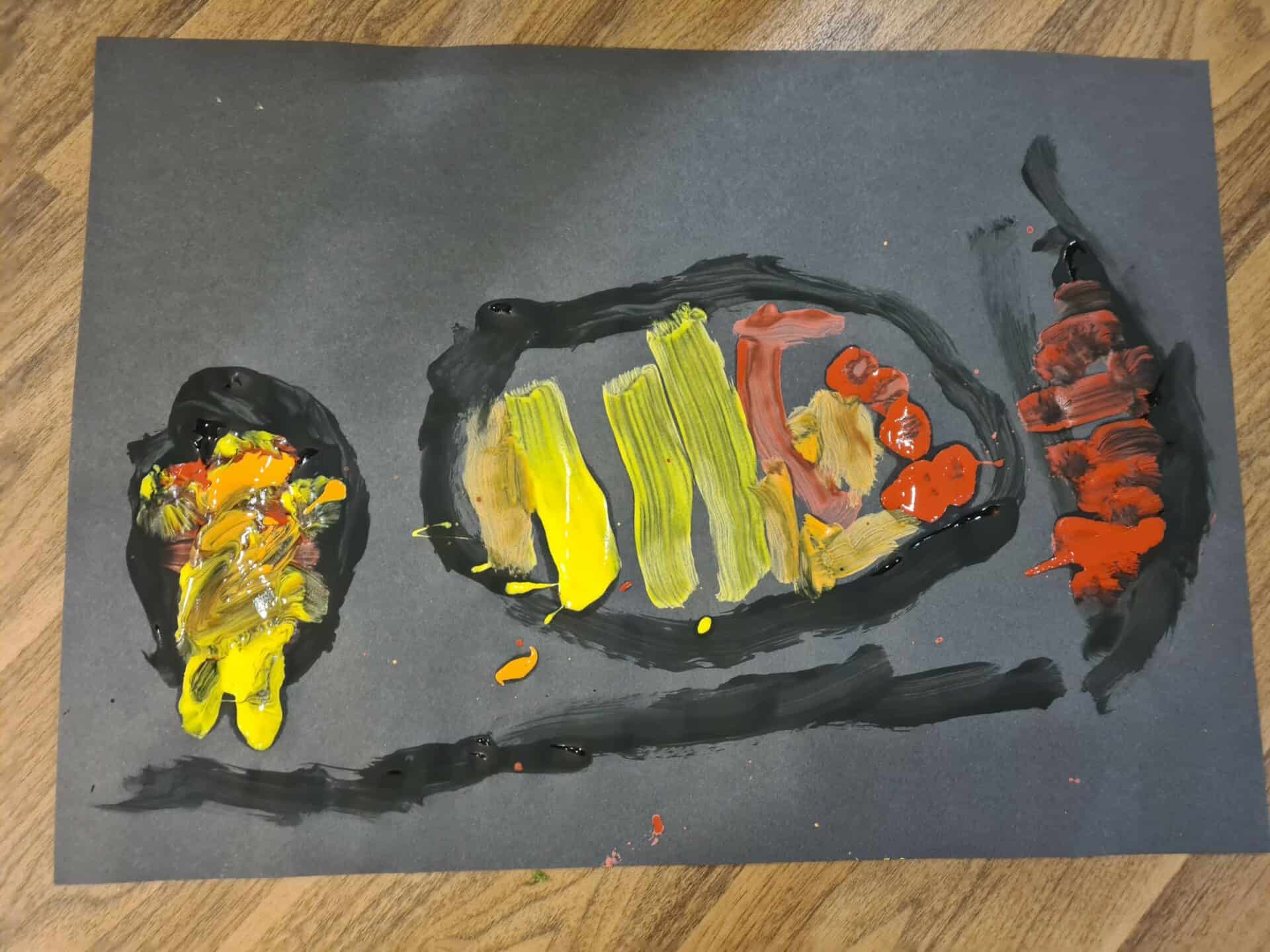 Bright and colourful children's painted artwork of a fish on black paper, showcasing creativity and early childhood development at Thrive Childcare.