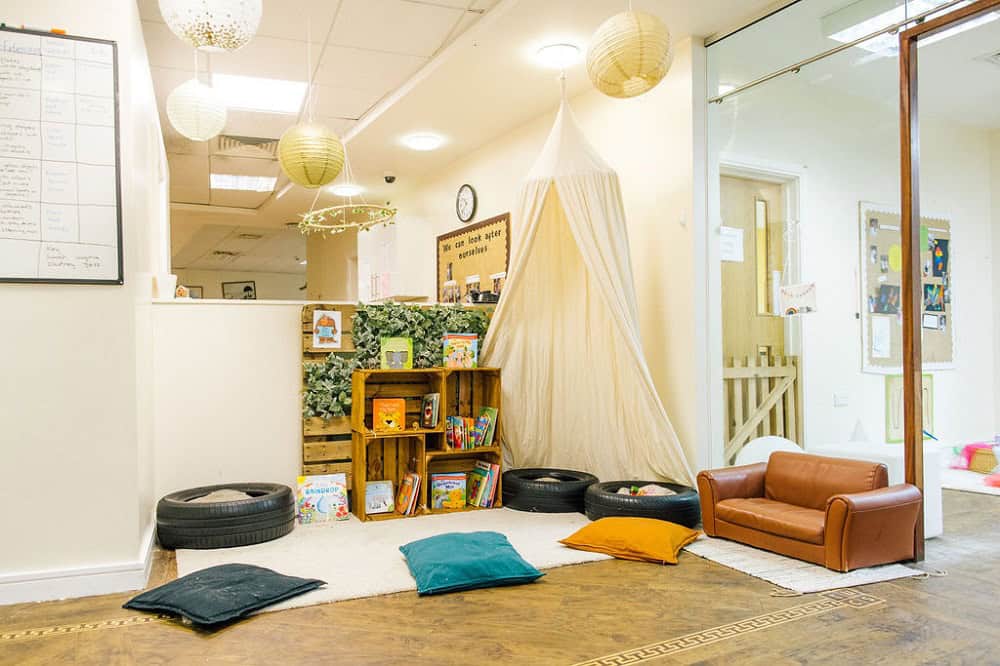 Bright and welcoming childcare play area with cosy reading nook, soft cushions, and kids' books, fostering a nurturing environment for early learning and child development at Thrive Childcare.